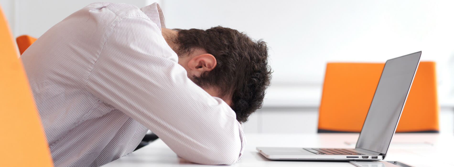 Man burying his head in his arms in front of his laptop.