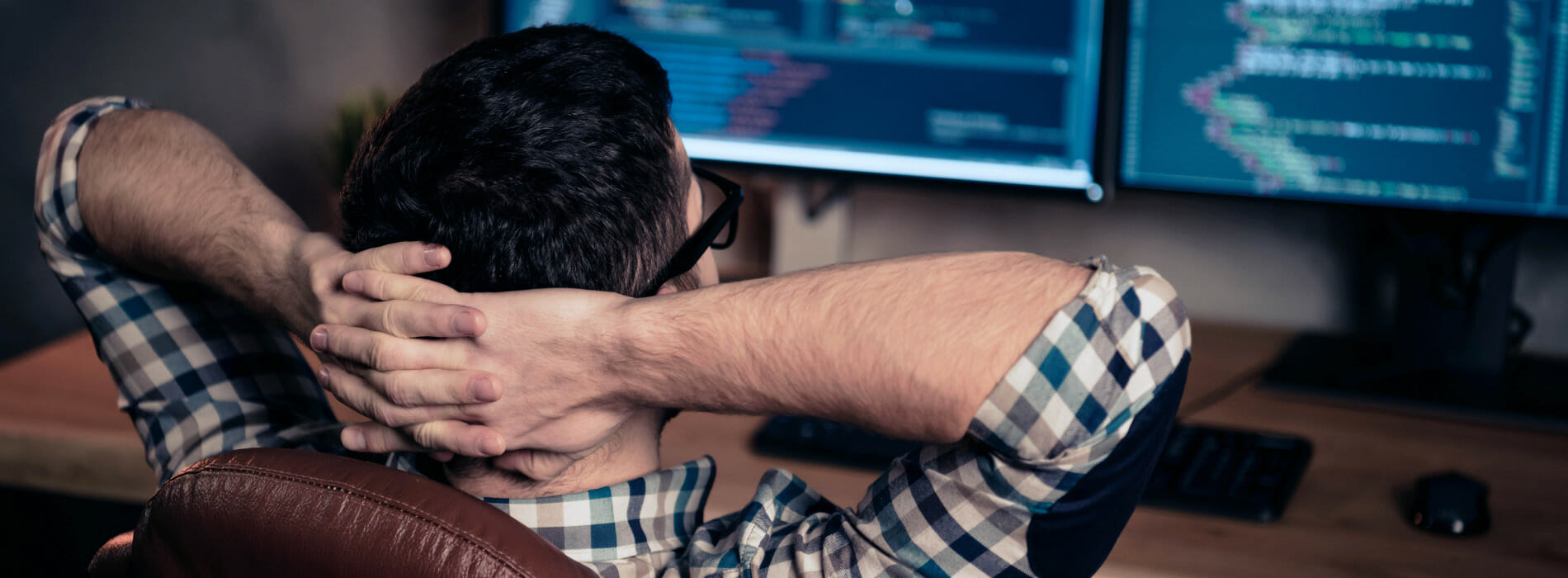 Man resting with his hands behind his head in front of a computer monitor.