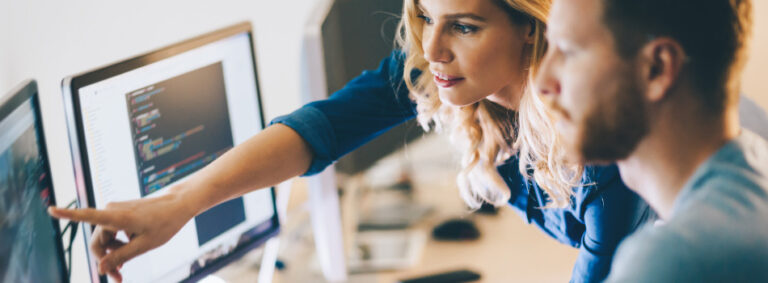 Colleagues look at a computer monitor in a bright office space.