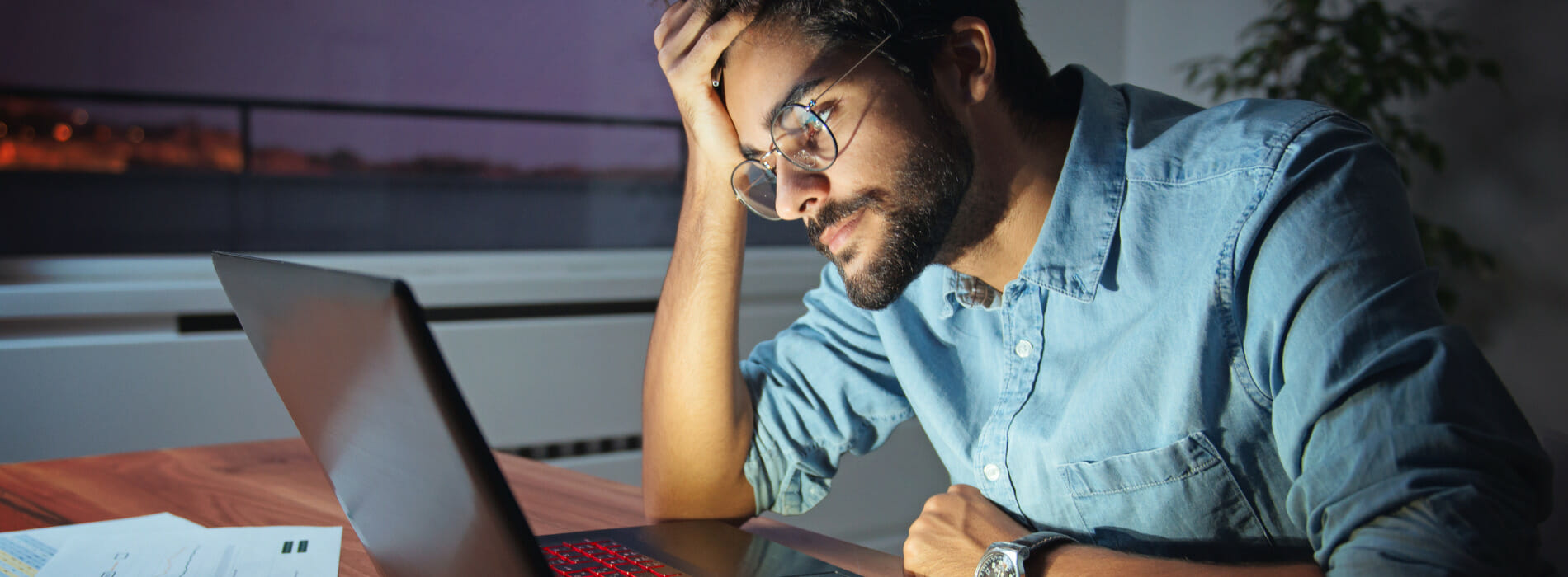 Man staring at his laptop screen with his head resting on his hand.