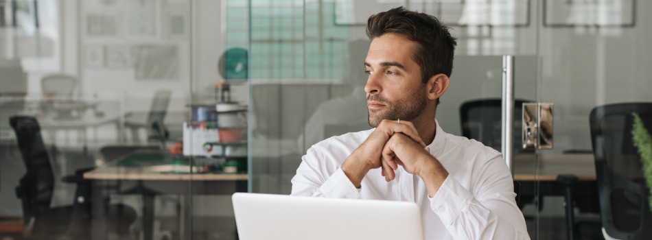 Office worker in front of a laptop, looking off to the left.