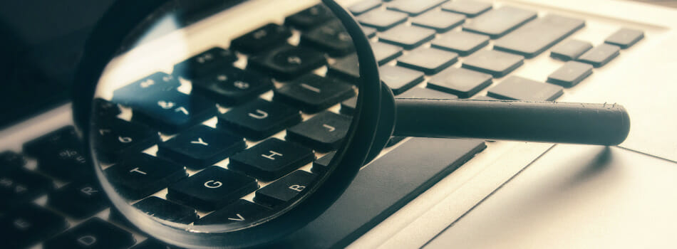 Image of a magnifying glass resting on a laptop keyboard.