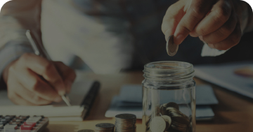 a person writing in a notebook with their right hand and putting a coin in a jar with their left hand